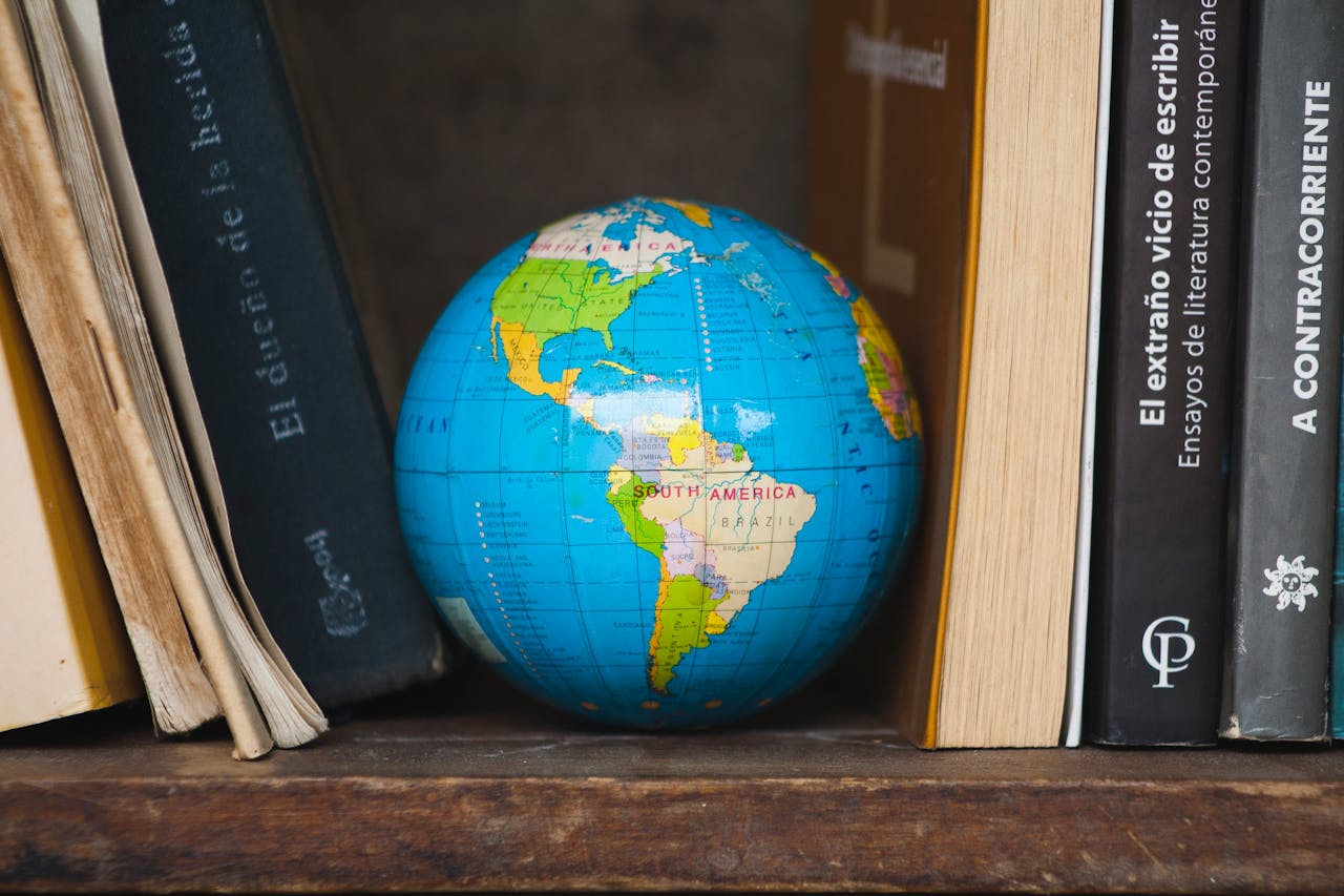 A vibrant globe nestled between classic books on a wooden shelf, highlighting South America.
